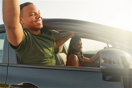 front seat - Young man leaning out of car window smiling, arms raised Stock Photo - Premium Royalty-Free, Code: 649-08144747