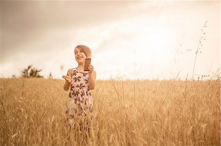 Girl using smartphone whilst laughing in wheat field Stock Photo - Premium Royalty-Free, Code: 649-08179895