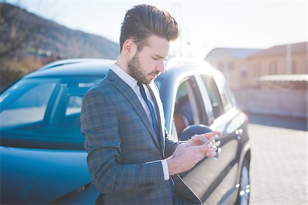 Young businessman leaning against car reading smartphone texts Foto de stock - Sin royalties Premium, Código: 649-08180079