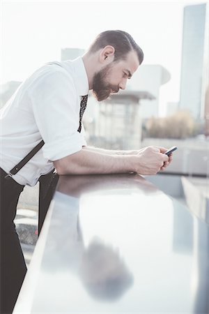 Stylish businessman reading smartphone text leaning against office balcony Stock Photo - Premium Royalty-Free, Code: 649-08237684