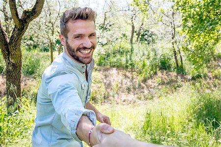 simsearch:649-08239088,k - Young man holding hand looking at camera smiling Stock Photo - Premium Royalty-Free, Code: 649-08239085