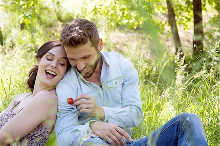 simsearch:649-08239088,k - Young couple sitting back to back on grass holding strawberry smiling Stock Photo - Premium Royalty-Free, Code: 649-08239080