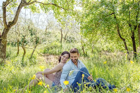 simsearch:649-08239088,k - Young couple sitting back to back on grass looking down smiling Stock Photo - Premium Royalty-Free, Code: 649-08239081