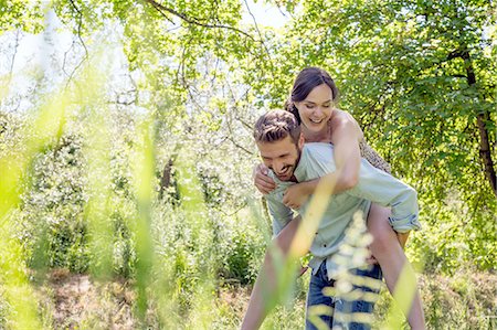 simsearch:649-08239088,k - View through foliage of young man giving young woman piggyback Stock Photo - Premium Royalty-Free, Code: 649-08239082