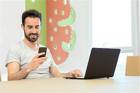 Young male designer texting on smartphone at boardroom table Stock Photo - Premium Royalty-Free, Code: 649-08306338