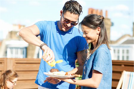 Mid adult man squirting mustard on burger at rooftop party Foto de stock - Sin royalties Premium, Código: 649-08306623