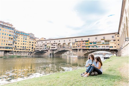 Lesbian couple sitting together on riverbank looking at digital camera in front of Ponte Vecchio and river Arno, Florence, Tuscany, Italy Stock Photo - Premium Royalty-Free, Code: 649-08306724