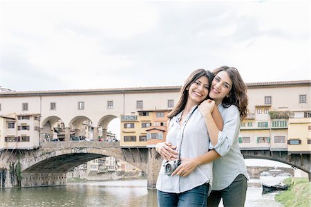 Lesbian couple standing hugging in front of Ponte Vecchio and river Arno looking at camera smiling, Florence, Tuscany, Italy Stock Photo - Premium Royalty-Free, Code: 649-08306726
