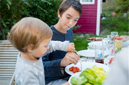 simsearch:649-07648247,k - Teenage boy helping female toddler eat food at garden barbecue Stock Photo - Premium Royalty-Free, Code: 649-08381243