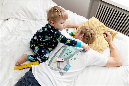 sleepy - Young boy playing with toy car on back of fathers tshirt in bed Stock Photo - Premium Royalty-Free, Code: 649-08381269