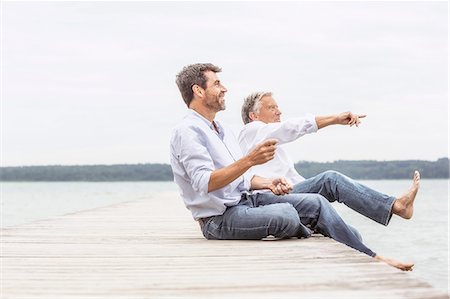 Two men sitting on pier, throwing stones, smiling Stock Photo - Premium Royalty-Free, Code: 649-08381571