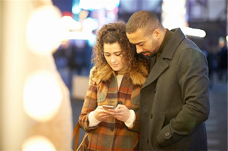 Couple looking at smartphone, outdoors, at night Stock Photo - Premium Royalty-Free, Code: 649-08423095