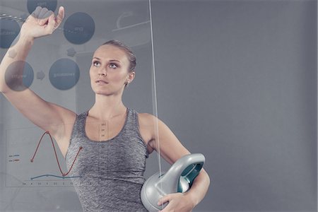 Young woman with kettle bell studying chart on glass wall, grey background Stock Photo - Premium Royalty-Free, Code: 649-08479920