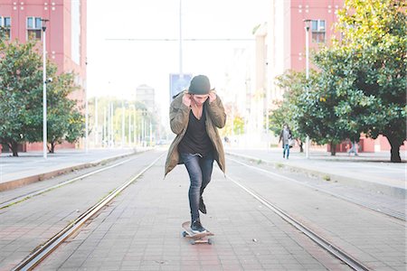 simsearch:649-07710443,k - Young male skateboarder adjusting earphones whilst skateboarding on tramway Stock Photo - Premium Royalty-Free, Code: 649-08548909