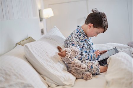 Boy in pyjamas using digital tablet in bed Stock Photo - Premium Royalty-Free, Code: 649-08543546