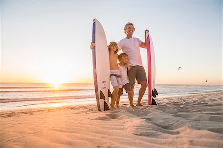 Full length view of father and sons standing on beach holding surfboard at sunset Stock Photo - Premium Royalty-Free, Code: 649-08543786