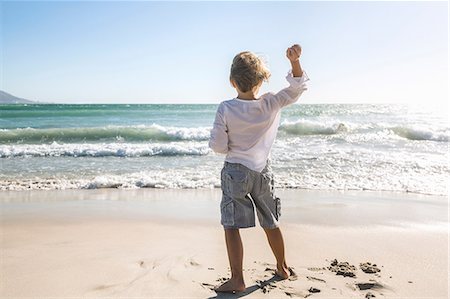 Full length rear view of boy on beach throwing stones into ocean Stock Photo - Premium Royalty-Free, Code: 649-08543805
