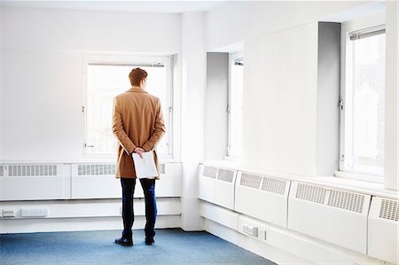 Rear view of man in empty office, hands behind back looking out of window Stock Photo - Premium Royalty-Free, Code: 649-08576342
