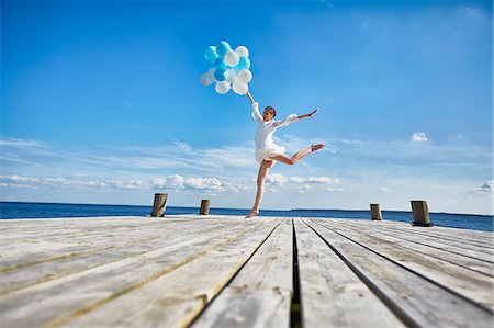 Young woman dancing on wooden pier, holding bunch of balloons Foto de stock - Royalty Free Premium, Número: 649-08576428