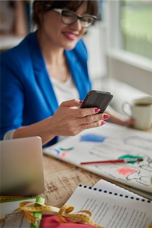 simsearch:649-06845199,k - Woman in design studio sitting at desk looking at smartphone smiling Stock Photo - Premium Royalty-Free, Code: 649-08576836