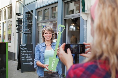 simsearch:614-07806416,k - Friend photographing woman in front of shop holding open sign Photographie de stock - Premium Libres de Droits, Code: 649-08576887