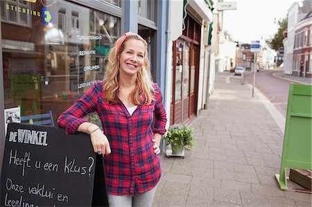 simsearch:614-07806416,k - Woman in front of shop leaning against a-frame looking at camera smiling Photographie de stock - Premium Libres de Droits, Code: 649-08576881