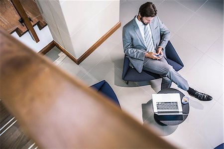 simsearch:649-07520071,k - High angle view of businessman in lobby looking down at smartphone Stock Photo - Premium Royalty-Free, Code: 649-08576936