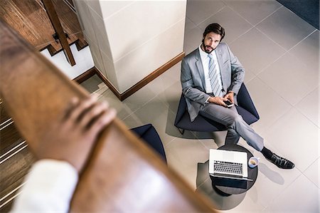 simsearch:649-07520071,k - High angle view of businessman in lobby holding smartphone looking up Stock Photo - Premium Royalty-Free, Code: 649-08576937