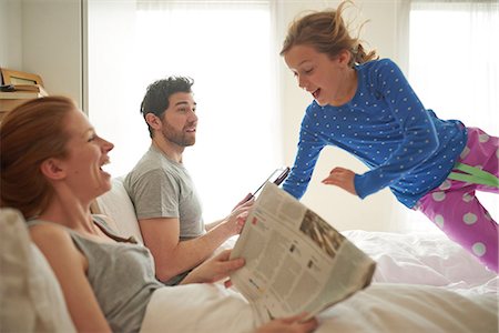 surprised - Mid adult couple reading broadsheet whilst daughter leaps on bed Stock Photo - Premium Royalty-Free, Code: 649-08577247