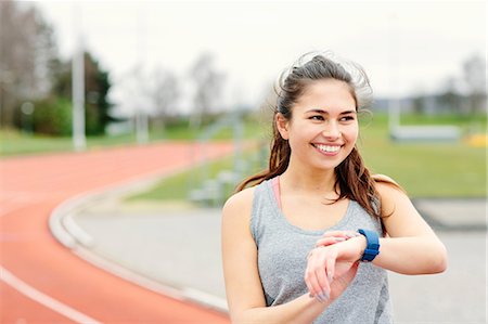 Young woman beside running track, checking watch, smiling Stock Photo - Premium Royalty-Free, Code: 649-08577265