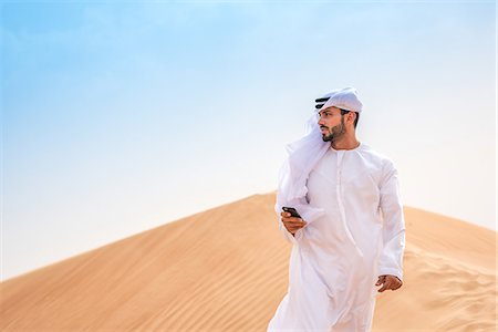 dubai traditional clothing for men - Middle eastern man wearing traditional clothes using smartphone on desert dune, Dubai, United Arab Emirates Stock Photo - Premium Royalty-Free, Code: 649-08577575