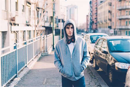 Man in urban area wearing hooded top and headphones looking at camera Stock Photo - Premium Royalty-Free, Code: 649-08577901