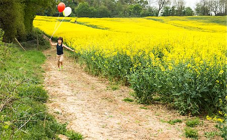 farm and boys - Boy running along yellow flower field track pulling red and white balloons Stock Photo - Premium Royalty-Free, Code: 649-08661115