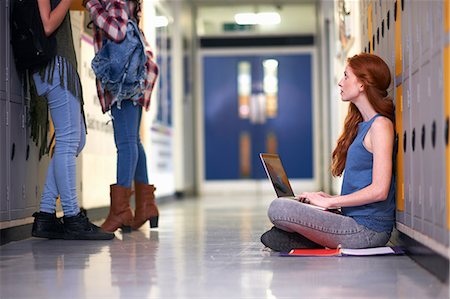 simsearch:614-07031973,k - Young female college student sitting on locker room floor looking up whilst typing on laptop Stock Photo - Premium Royalty-Free, Code: 649-08702359