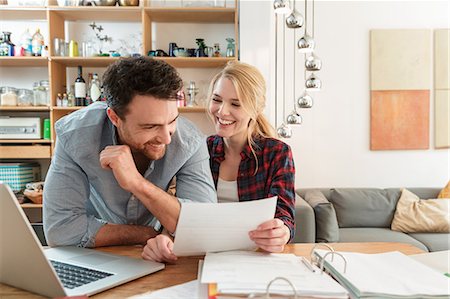 Couple with laptop looking at paperwork smiling Stock Photo - Premium Royalty-Free, Code: 649-08714489