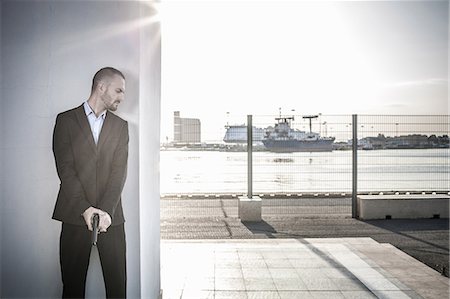 Man in business attire behind wall at harbour poised with handgun, Cagliari, Sardinia, Italy Stock Photo - Premium Royalty-Free, Code: 649-08714600