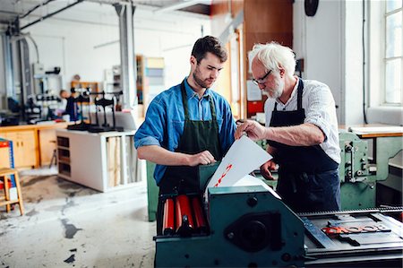 Senior craftsman/technician supervising young man on letterpress machine in book arts workshop Stock Photo - Premium Royalty-Free, Code: 649-08744894