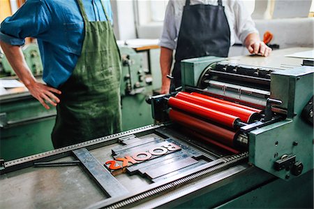 printer - Senior craftsman/technician supervising young man on letterpress machine in book arts workshop, mid section Stock Photo - Premium Royalty-Free, Code: 649-08744890