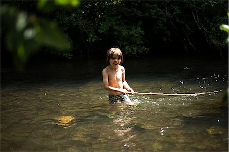 photos of little boy fishing - Boy waist deep in water holding stick Foto de stock - Sin royalties Premium, Código: 649-08745637