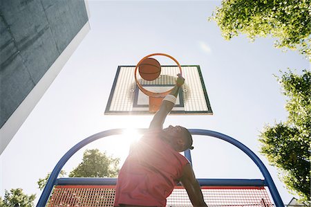 Young male basketball player throwing ball in sunlit basketball hoop Stock Photo - Premium Royalty-Free, Code: 649-08765735