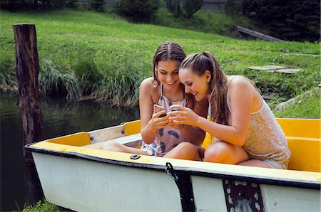 simsearch:649-07804673,k - Two young female friends reading smartphone texts in rowing boat on lakeside Photographie de stock - Premium Libres de Droits, Code: 649-08765999
