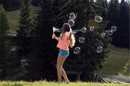 Young woman blowing bubbles in field, Sattelbergalm, Tirol, Austria Stock Photo - Premium Royalty-Free, Code: 649-08824154