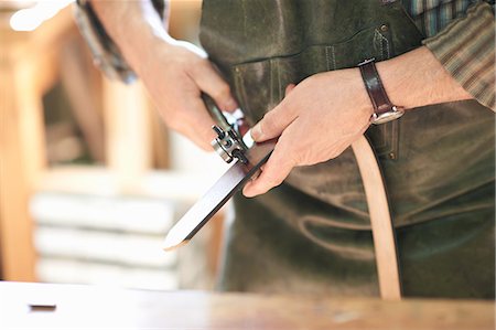Male worker in leather workshop, punching holes in leather belt, mid section, close-up Stock Photo - Premium Royalty-Free, Code: 649-08824419