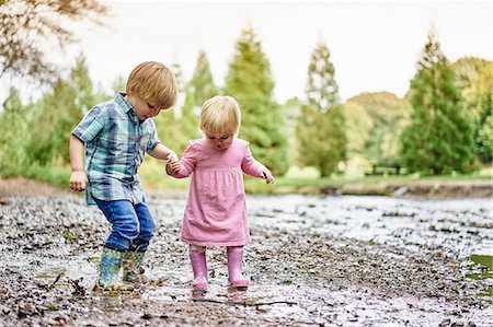 Brother and sister holding hands splashing in muddy puddle Stock Photo - Premium Royalty-Free, Code: 649-08824814