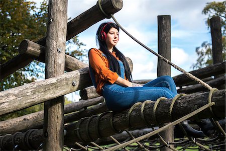 simsearch:614-08392638,k - Young woman sitting on wooden climbing frame, wearing headphones Stock Photo - Premium Royalty-Free, Code: 649-08824891