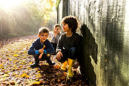 Three young boys, sitting against fence, surrounded by autumn leaves Stock Photo - Premium Royalty-Free, Code: 649-08839964