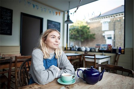 simsearch:614-08392638,k - Young woman sitting in cafe, cup of tea and teapot on table, thoughtful expression Foto de stock - Sin royalties Premium, Código: 649-08840431