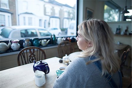 simsearch:614-08392638,k - Young woman sitting in cafe, cup of tea and teapot on table, looking out of window Foto de stock - Sin royalties Premium, Código: 649-08840432