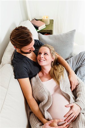 pregnant couple couch - Pregnant mid adult couple touching pregnant stomach on sofa Foto de stock - Sin royalties Premium, Código: 649-08860065