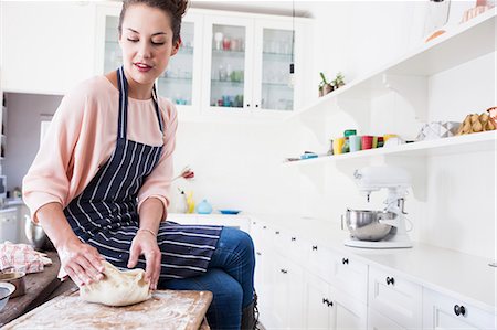 Young woman sitting on kitchen counter shaping dough Stock Photo - Premium Royalty-Free, Code: 649-08894282